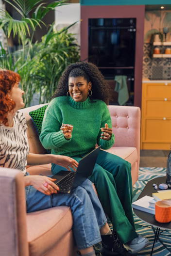 Two women laughing and talking while one is using a laptop